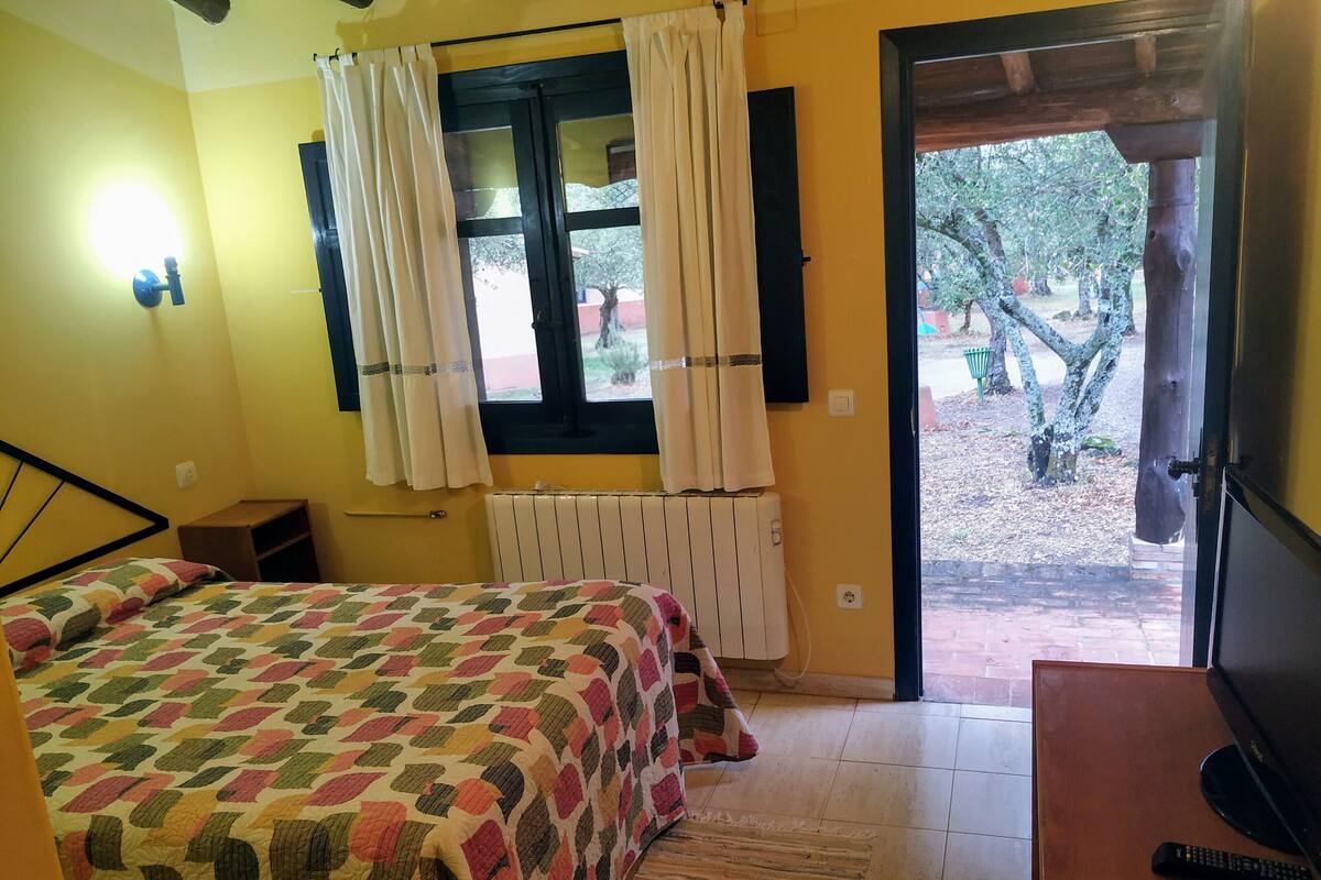 Ein Schlafzimmer mit Bett, einem fenster mit Vorhängen, einer Heizung, einem Holzboden und einem Fernsehtisch mit Fernbedienung.