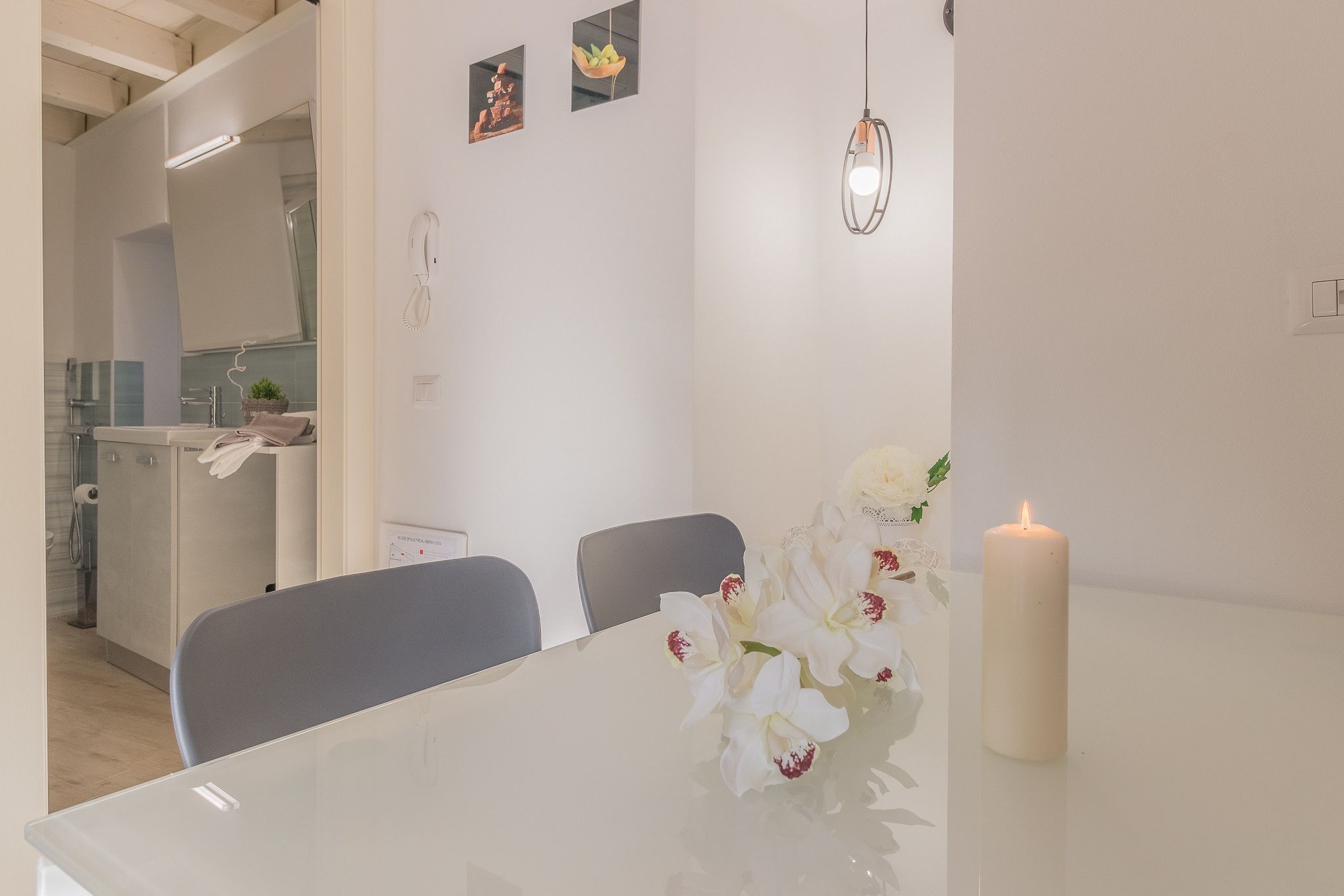 Un'area pranzo moderna con un tavolo bianco, sedie e una candela accesa.