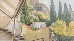 A stone building with a small window, a staircase, and a view of trees and a hill. - Pretty Home (Varenna)