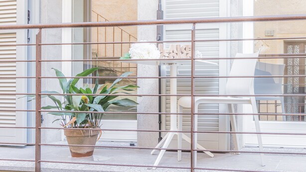 A balcony with a potted plant, a white chair, and a table. - Pretty Home (Varenna)