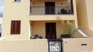 Ein zweistöckiges Gebäude mit einem Balkon im oberen Stockwerk, einer Tür im Erdgeschoss und einem kleinen Fenster im oberen Stockwerk.