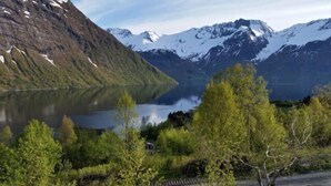 A mountain lake with snow-capped peaks in the background and a forested foreground. - Magnificent landscape, fjords and mountains and an unic sommer house. (Norangsfjorden)