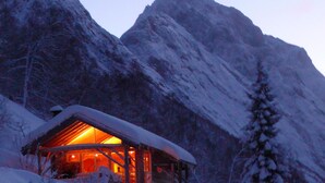 A wooden cabin with a warm interior light, surrounded by snow-covered mountains. - Magnificent landscape, fjords and mountains and an unic sommer house. (Norangsfjorden)