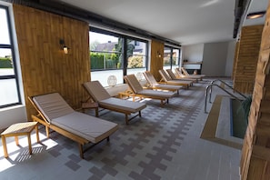 Een zonnedoek met meerdere lounge stoelen gerangschikt in rijen, grote ramen en een betegelde vloer.