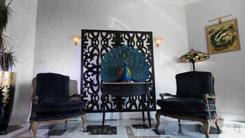 A room with a peacock sculpture, two armchairs, a lamp, and a painting on the wall.