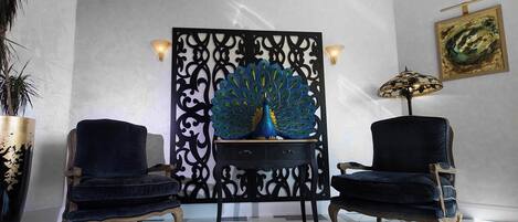 A room with a peacock sculpture, two armchairs, a lamp, and a painting on the wall.