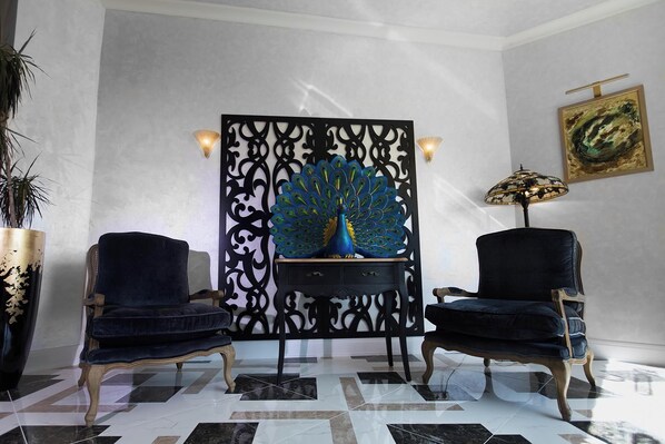 A room with a peacock sculpture, two armchairs, a lamp, and a painting on the wall. - Hotel Westermann (Oelde)