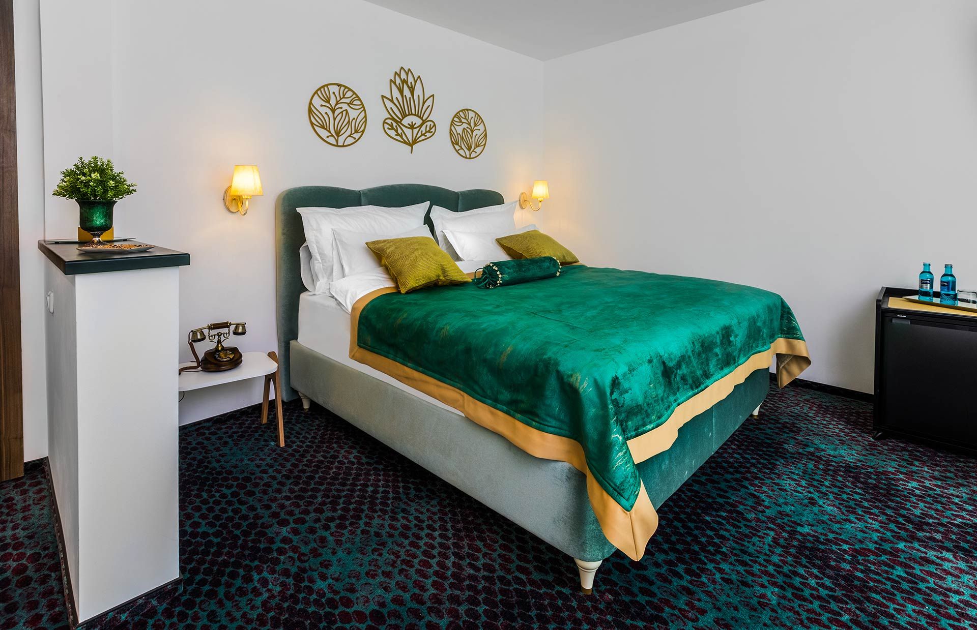 Una habitación de hotel con cama, mesitas de noche, un escritorio y decoración en la pared.