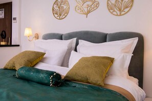 A bed with white and green pillows, a teal bedspread, and a wall with decorative leaf patterns. - Hotel Westermann (Oelde)
