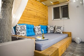 A cozy room with a wooden bed, blue cushions, and a small table with a bottle and bowl. - NK Apartments (Kissamos)