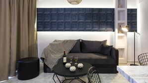 Un salon moderne avec un canapé gris foncé, une table ronde noire sur laquelle se trouvent une bouteille et des verres, et un luminaire suspendu au design original.