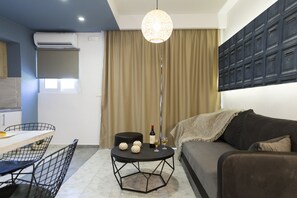 A modern living room with a dining area, a black sofa, a round table with decorative items, and a pendant light. - NK Apartments (Kissamos)