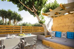 An outdoor patio with a table, chairs, and a wooden bench. - NK Apartments (Kissamos)