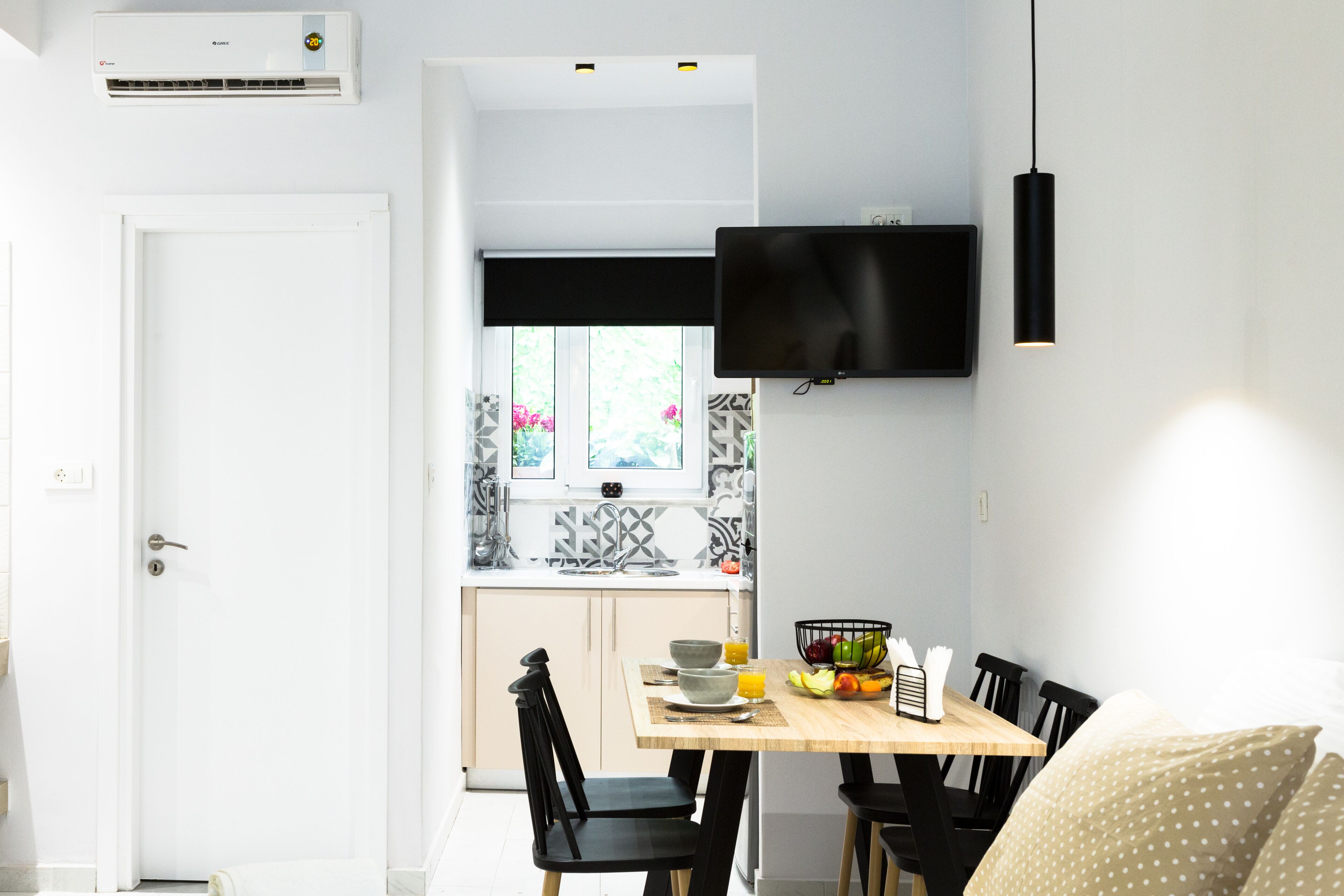 A modern kitchen with a flat-screen TV, a dining table with chairs, and a window with a view of greenery.