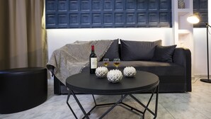 Un salon moderne avec un canapé de couleur sombre, une table ronde noire agrémentée d’objets décoratifs, une bouteille de vin et deux verres.