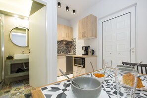A modern kitchen with a dining area, featuring a tiled backsplash, wooden cabinets, and a coffee maker. - NK Apartments (Kissamos)