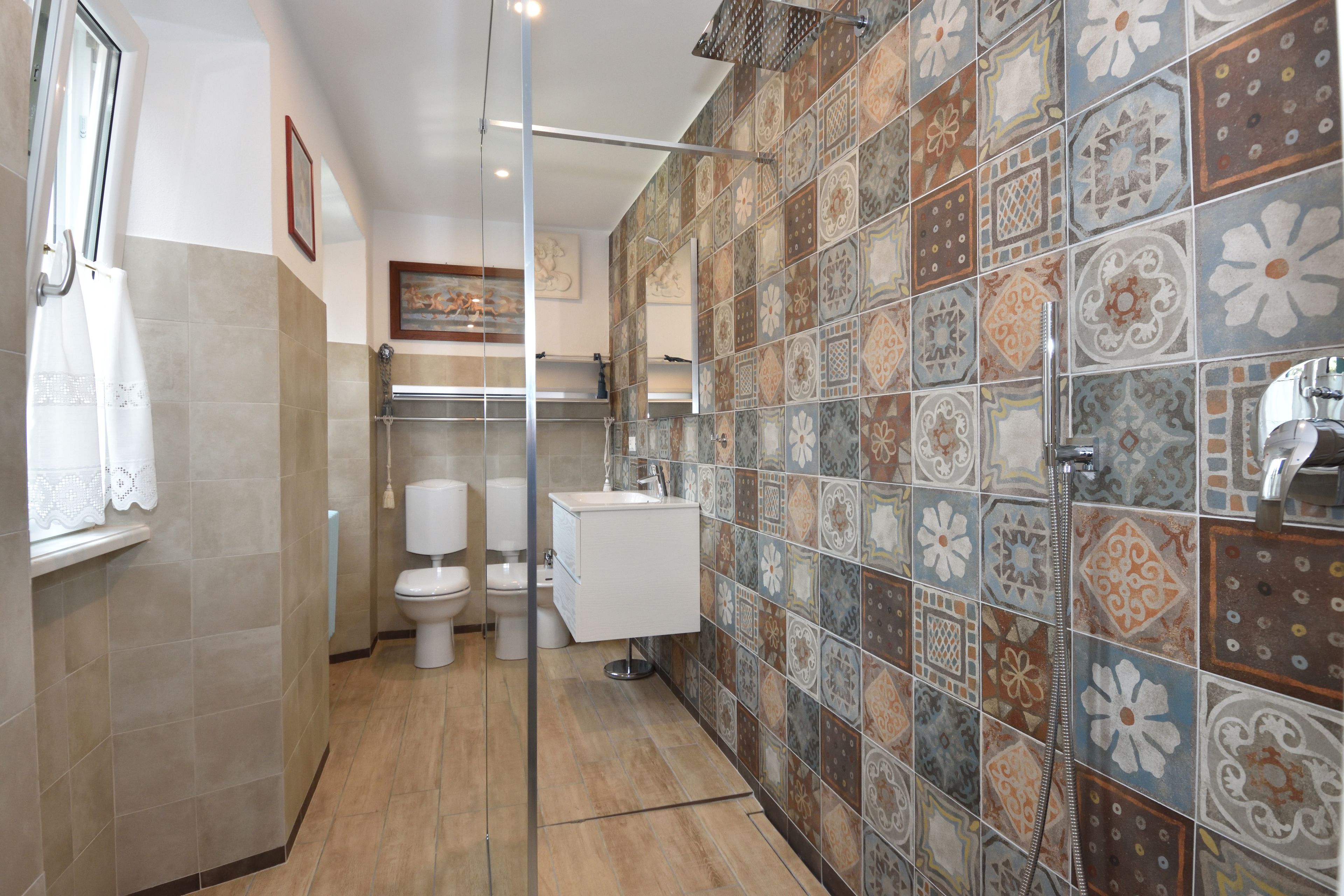 Une salle de bain équipée d’une douche, de toilettes et d’un lavabo, avec un mur recouvert de carreaux décorés d’un motif floral.