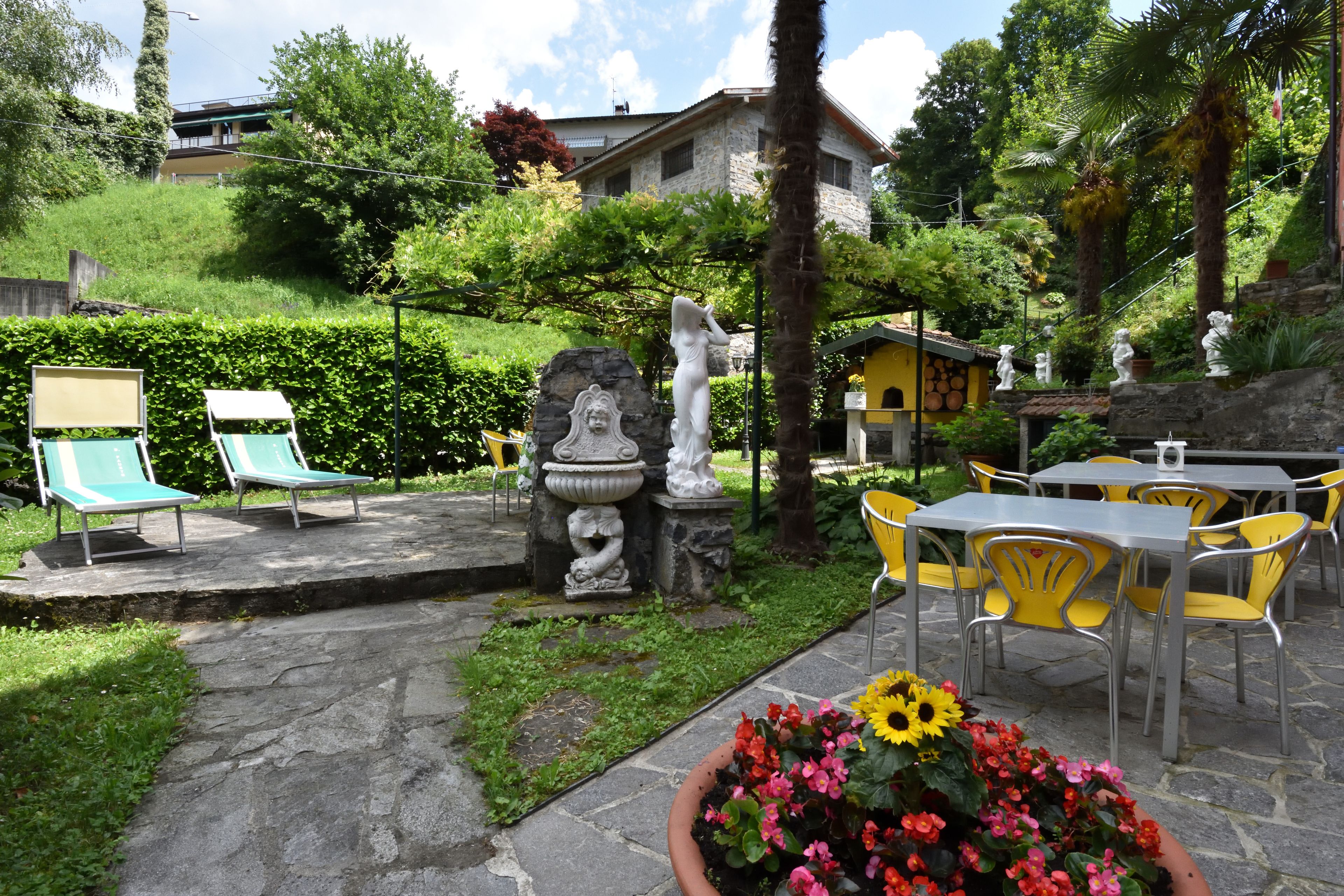 A garden patio with stone flooring, outdoor seating, and decorative statues.