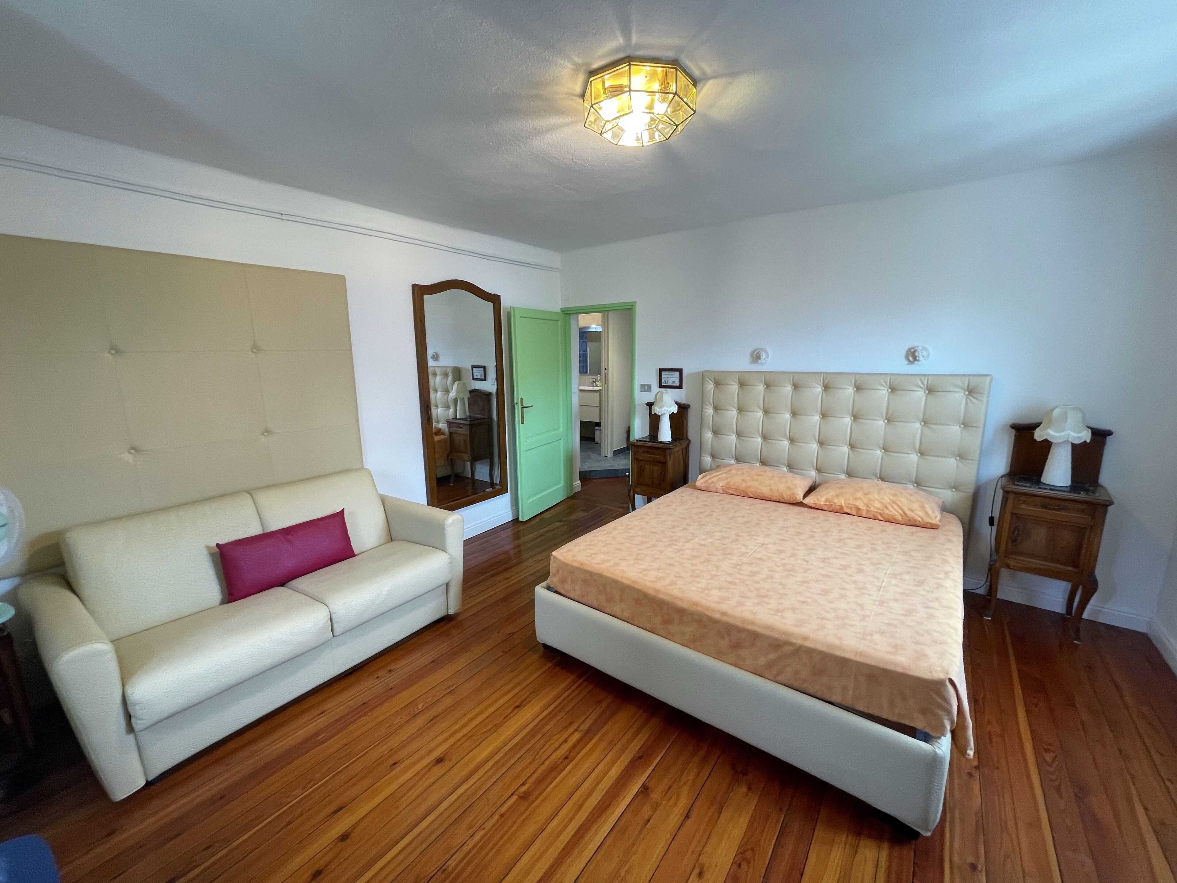 Une chambre à coucher comprenant un lit, un canapé, une table de chevet, un miroir et un luminaire au plafond.