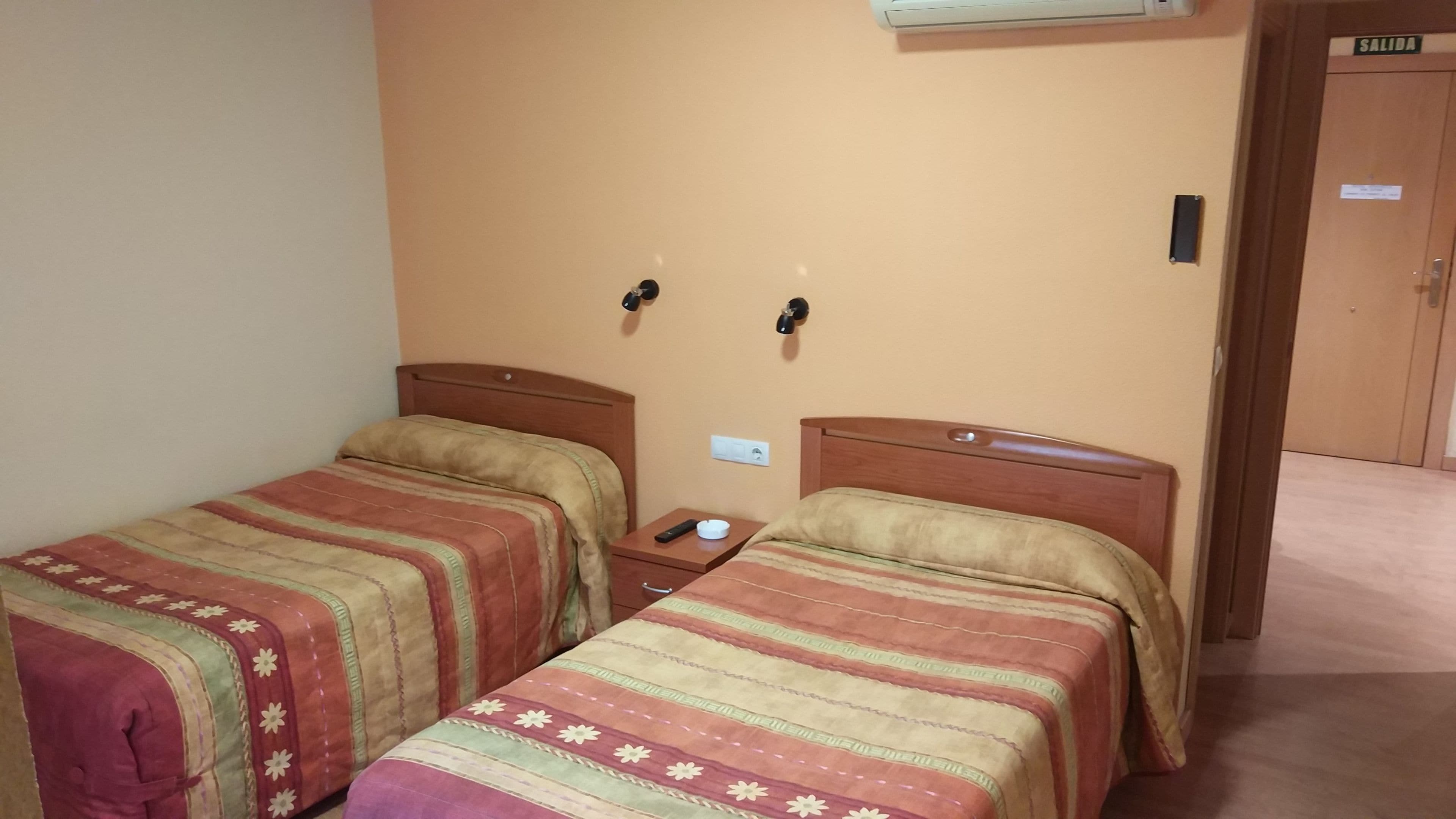 Una habitación de hotel con dos camas individuales, una mesita de noche con un control remoto y un equipo de aire acondicionado en la pared.