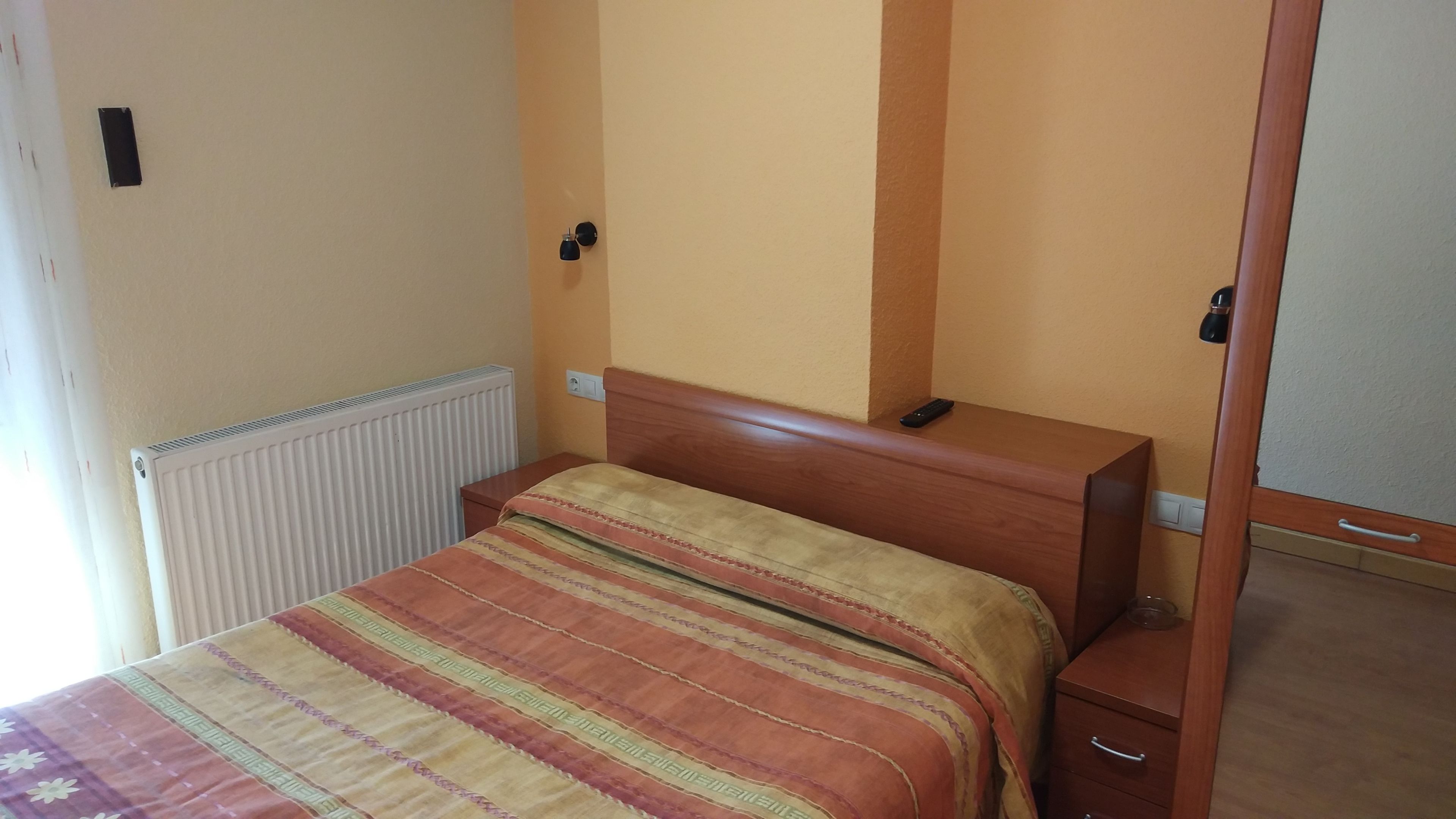 Un dormitorio con cama, una mesita de noche de madera, un radiador y una puerta.