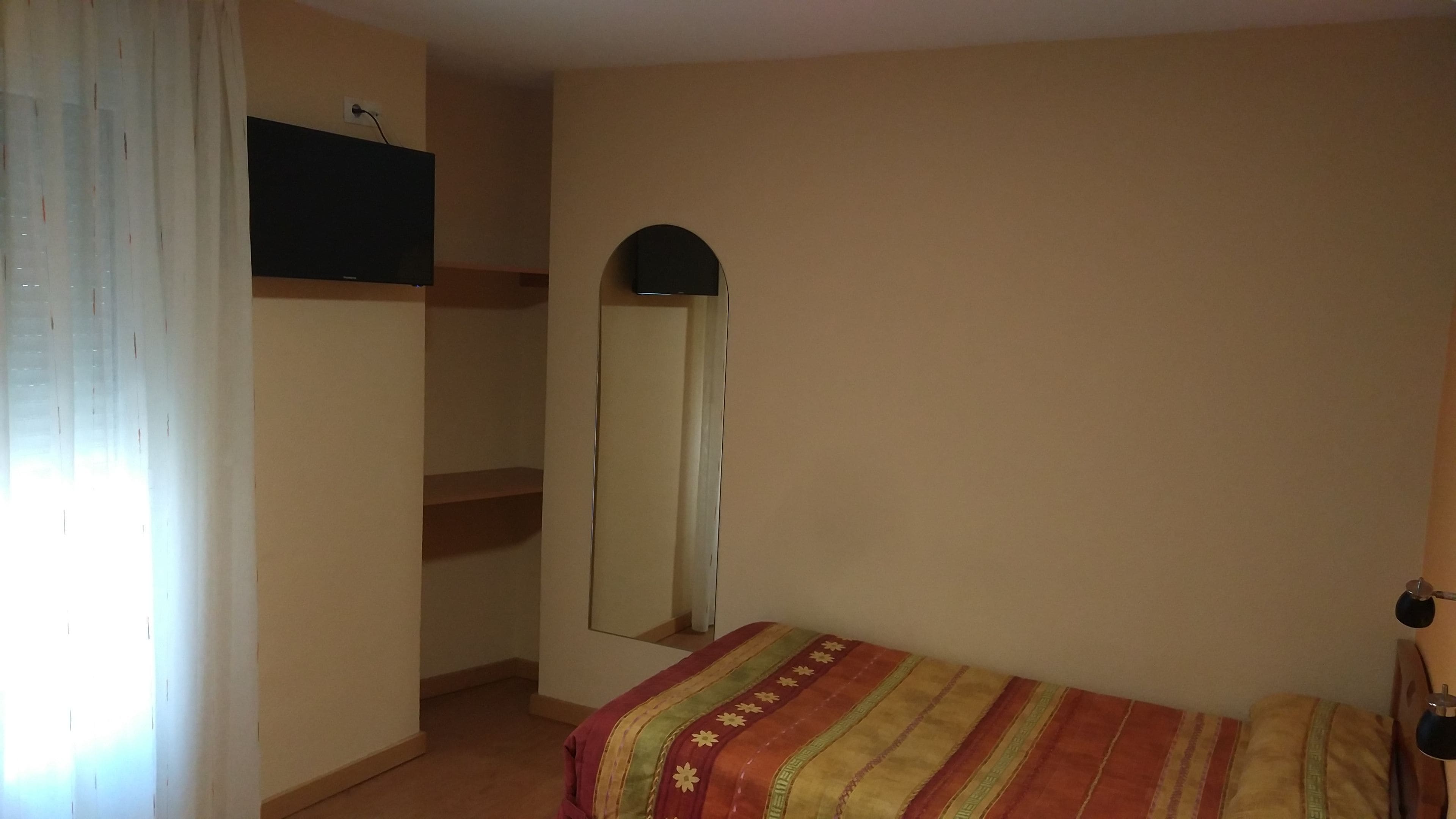 Un dormitorio con cama, espejo, armario y ventana con cortinas.