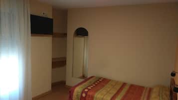 Un dormitorio con cama, espejo, armario y ventana con cortinas.
