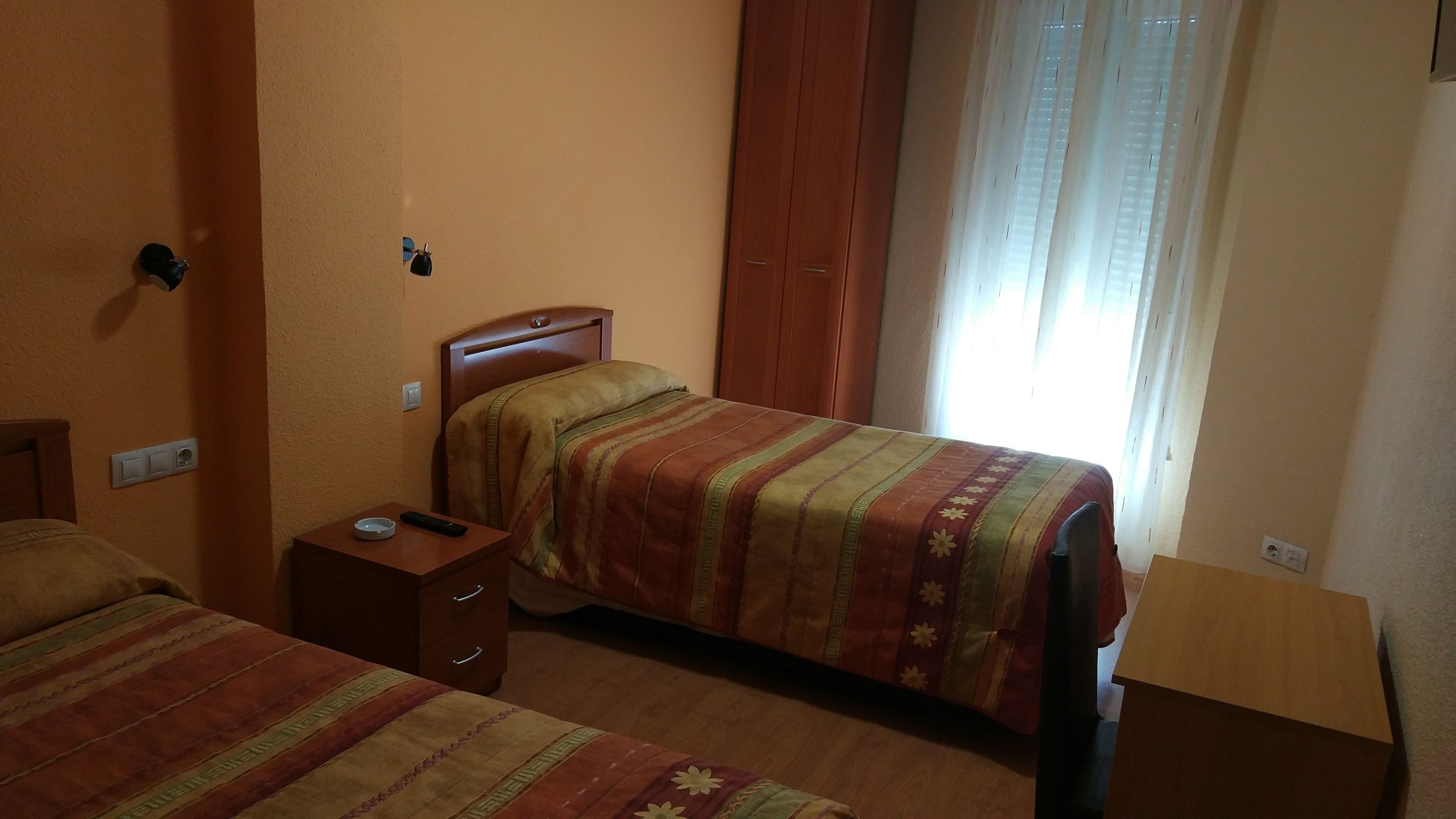 Una habitación de hotel con dos camas, una mesita de noche de madera, una mesilla auxiliar y una ventana con cortinas.