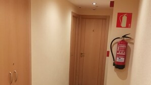 A hallway with wooden flooring, a fire extinguisher mounted on the wall, and a door at the end. - Hostal Hispanico II (Salamanca)