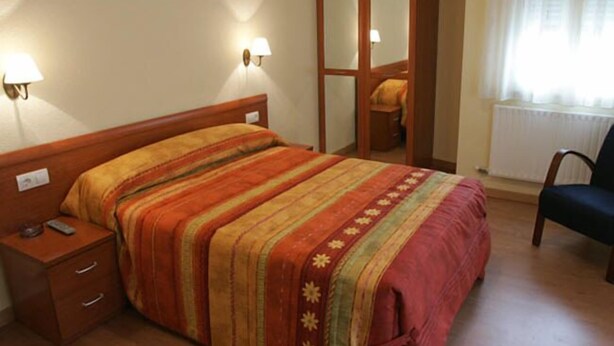A bedroom with a bed, nightstand, and a mirror. - Hostal Hispanico II (Salamanca)