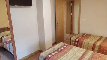 Una habitación pequeña y funcional con dos camas individuales, un armario de madera y una puerta que da a otra habitación.