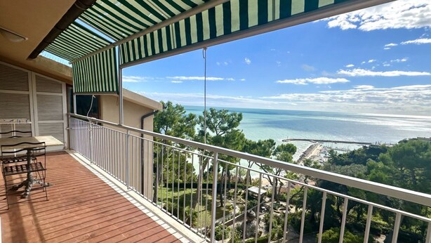 A balcony with a view of the sea, a dining table, and a covered area with a striped awning. - CASA DEL SOLE - Numana, wonderful sea view penthouse (Numana)