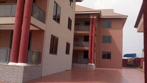A multi-story building with a tiled courtyard, large columns, and balconies. - Alpha's Court (Kumasi)