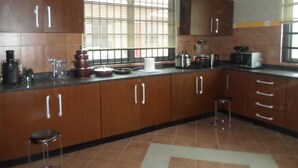 A kitchen with wooden cabinets, a window with blinds, and various kitchen appliances. - Alpha's Court (Kumasi)
