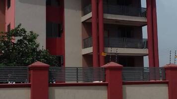 Un edificio de varios pisos con techo plano, balcones y un área de entrada pavimentada.