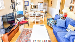 A living room with a TV, sofa, coffee table, and a dining area with chairs and a table. - Experience Tilghman Beach and Racquet Club Unit 309! 3 Bedroom Ocean View Condo. Pools, Tennis, Close to Main Street! (North Myrtle Beach)