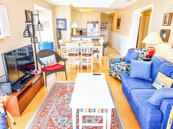 A living room with a TV, sofa, coffee table, and a dining area with chairs and a table.