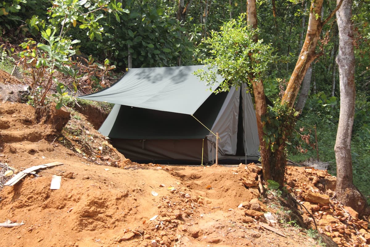 A tent set up in a forested area with a dirt ground and trees around.