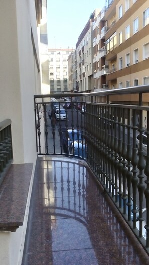 A narrow balcony with a metal railing overlooking a street with parked cars and a building in the background. - Hostal Granada (Salamanca)