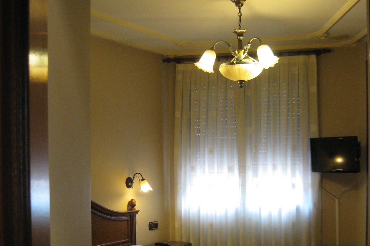 Ein Hotelzimmer mit einem Bett, einem Nachttisch, einer Lampe, einem Fernseher und einem Fenster mit Vorhängen.