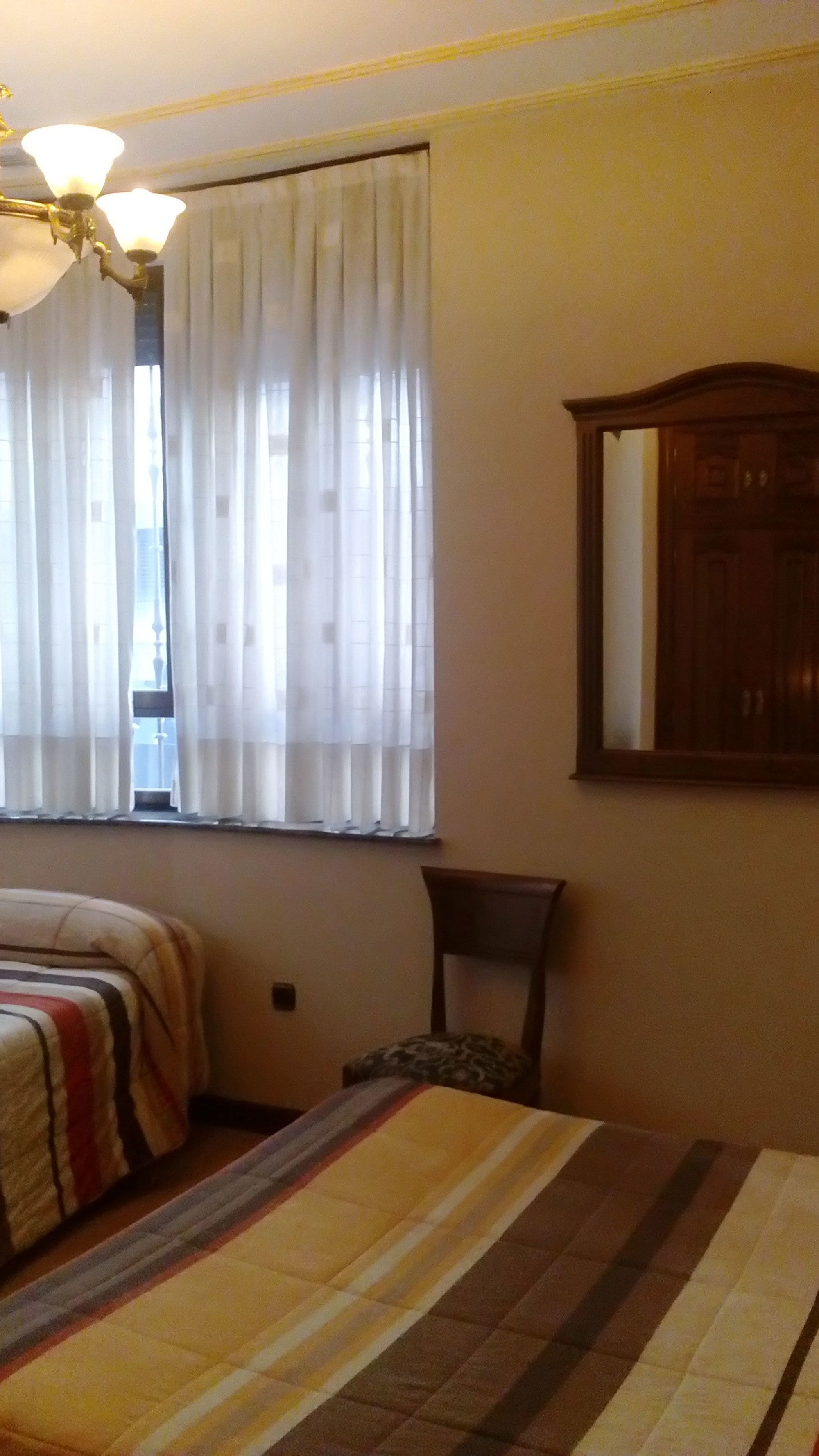 A bedroom with a bed, a chair, a wooden cabinet, and a window with curtains.