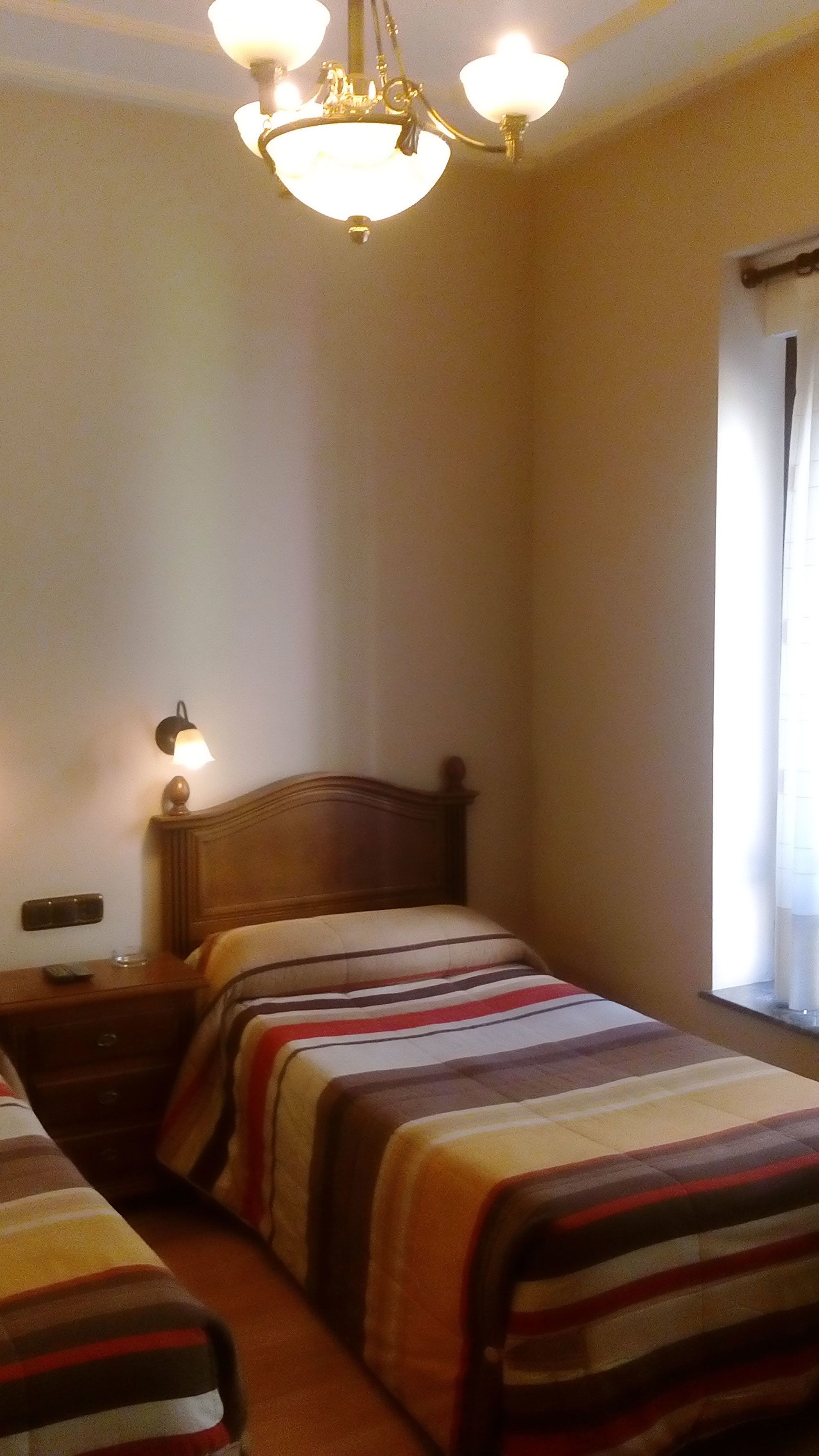 A hotel room with a wooden bed, a nightstand, a lamp, and a chandelier.