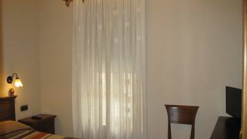 Una habitación de hotel con cama, una silla, escritorio con televisor y candelabro.