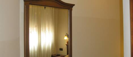 Habitación de hotel con un espejo grande, una silla, una mesita de noche con lámpara y un candelabro en el techo.