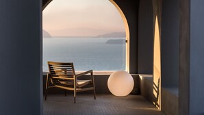A room with a view of the sea through an arched window, a wooden chair, and a spherical light fixture. - Arota Exclusive Villas (Santorini)