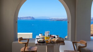 A table with breakfast items and a view of the sea through an arched window. - Arota Exclusive Villas (Santorini)