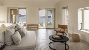 A modern living room with a white sofa, a round coffee table, and a view of the sea through large glass doors. - Arota Exclusive Villas (Santorini)