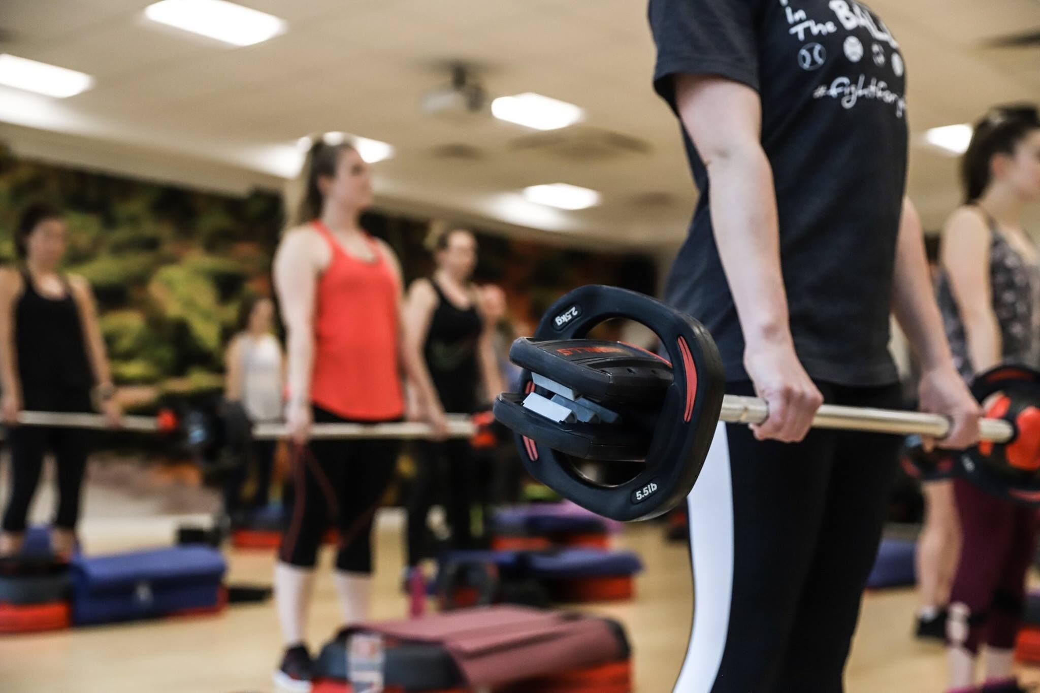 A person lifting a barbell in a gym with other people in the background.