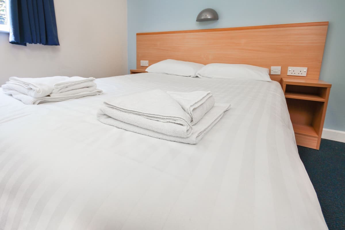 Un lit bien fait, avec du linge de lit blanc et des oreillers, une tête de lit en bois et une table de chevet avec une lampe.
