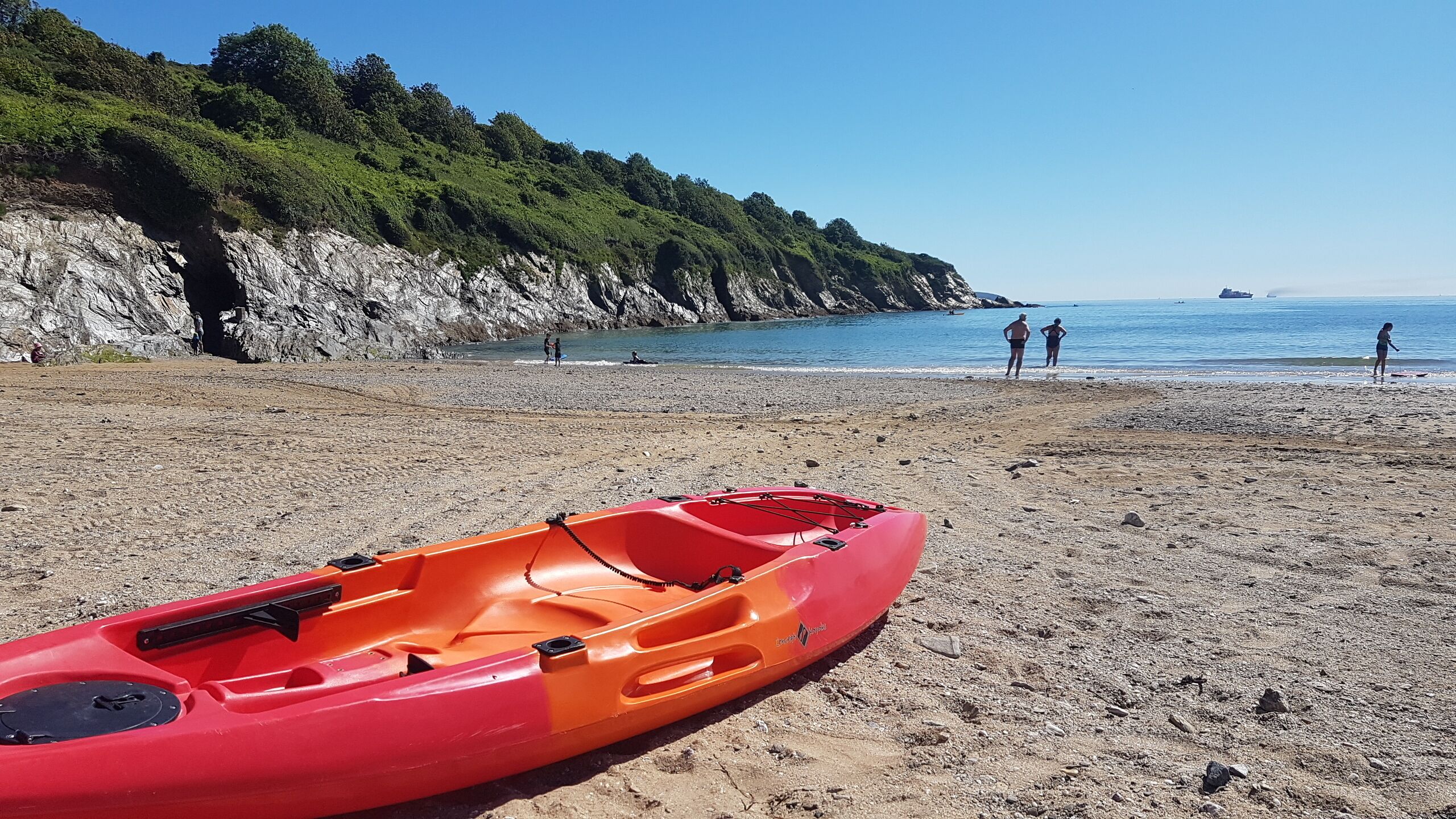 En röd kajak på en stenstrand med en klippa och havet i bakgrunden.